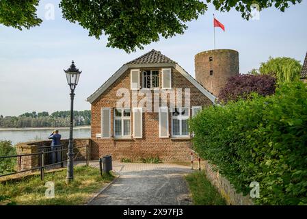 Ein Haus und ein Burgturm aus Ziegelsteinen mit Weg, Laterne und Fluss im Hintergrund, rheinpromenade direkt am Fluss mit alten Häusern Stockfoto