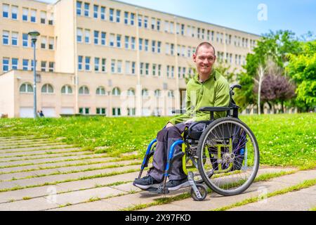 Vollbildnis eines kaukasischen jungen Mannes mit Zerebralparese im Rollstuhl allein auf dem Universitätscampus Stockfoto