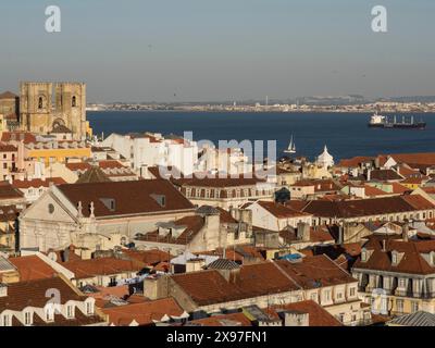 Panorama einer Stadt mit roten Dächern, großen historischen Gebäuden am Wasser und einem Frachtschiff im Hafen, Blick auf die Altstadt von Lissabon auf dem Stockfoto