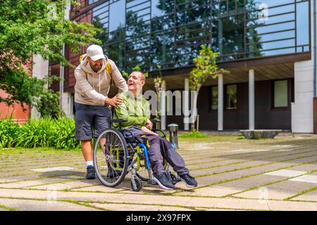 Foto in voller Länge von einem kaukasischen erwachsenen Mann mit besonderen Bedürfnissen und einem Freund, der auf dem Universitätscampus spaziert Stockfoto