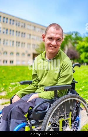 Vertikales Nahporträt eines im Rollstuhl lächelnden Mannes mit Zerebralparese auf dem Universitätscampus Stockfoto