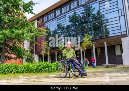 Langbildnis eines kakuasischen erwachsenen Mannes mit Zerebralparese, der in elektrischen Wheelchari am Eingang der Universität sitzt Stockfoto