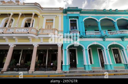 323 Fassaden von zweistöckigen, vielseitigen Gebäuden aus den frühen 1900er Jahren mit großen Balkonen im ersten Stock mit Blick auf den Parque Vidal Park. Santa Clara-Kuba. Stockfoto