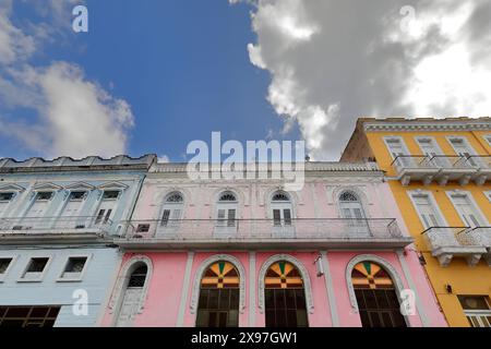 326 nach Westen gerichtete Kolonialgebäude, die auf der Ostseite des Parque Serafin Sanchez Park in Hellblau-Rosa-Safrangelb gestrichen sind. Sancti Spiritus-Kuba. Stockfoto
