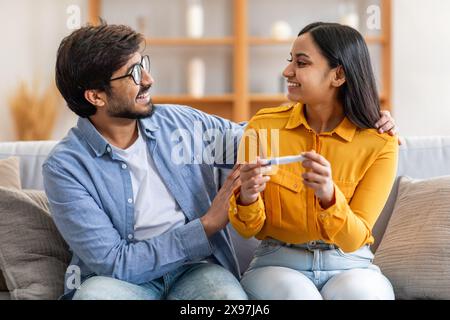 Glückliches Paar feiert positive Ergebnisse des Schwangerschaftstests im Wohnzimmer Stockfoto