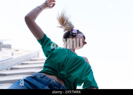Junge, fröhliche Frau, die in der Stadt tanzt und Kopfhörer trägt Stockfoto