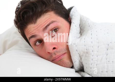 Nahaufnahme eines jungen Mannes im Bett unter der Decke mit unzufriedenem Gesicht Stockfoto