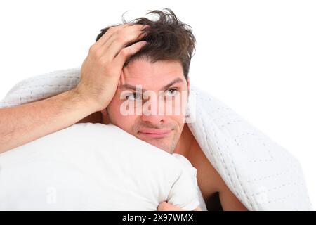 Nahporträt eines frustrierten, verärgerten jungen Mannes, der auf weißem Hintergrund im Bett liegt Stockfoto
