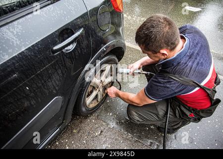 Der Mechaniker in Kiew, Ukraine, überprüft den Reifendruck unter Regen, eine gewöhnliche Sache während der 24-Stunden-Schicht Stockfoto