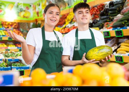 Positiv lächelnde Verkäuferin und Verkäufer in der Schürze, die frisches Obst im Geschäft anbietet Stockfoto