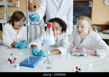 Gruppe ethnisch unterschiedlicher Mittelschüler, die Labormäntel und Schutzbrille tragen und chemische Reaktionen während des Experiments im Unterricht beobachten Stockfoto