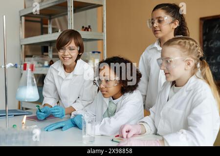 Multiethnische Gruppe von Jungen und Mädchen mit Labormänteln und Schutzbrille, die Experimente im Chemiekurs machen Stockfoto