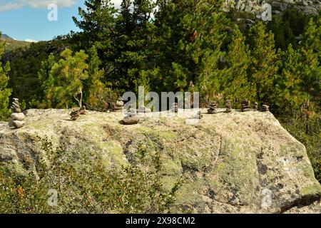 Mehrere kleine Steinpyramiden stapelten sich auf einem großen flachen Stein vor dem Hintergrund eines dichten Nadelwaldes. Naturpark Ergaki, Region Krasnojarsk, Stockfoto