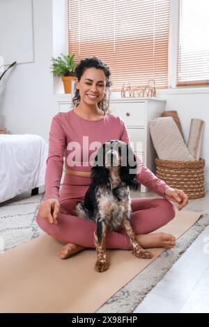 Sportliche junge afroamerikanische Frau mit Cocker Spaniel, die im Schlafzimmer meditiert Stockfoto