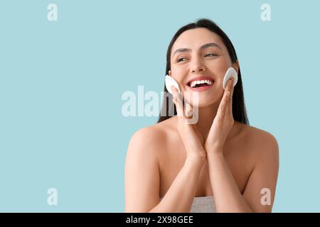 Glückliche junge Frau im Handtuch mit Wattepads zum Entfernen von Make-up auf blauem Hintergrund Stockfoto