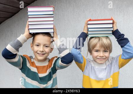 Zwei lustige 8-Jährige halten einen Stapel Bücher auf den Kopf. Zurück zur Schule. Tag Buchen. Lesen Sie mit Freude. Lesekonzept, pädagogisches Stockfoto