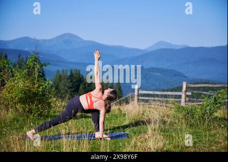 Frau übt Yoga im Freien in den Bergen in einer ruhigen, natürlichen Umgebung. Frauen, die Yoga spielen, posieren auf der Matte, vor dem Hintergrund der wunderschönen Berglandschaft bei Sonnenauf- oder -Untergang. Stockfoto