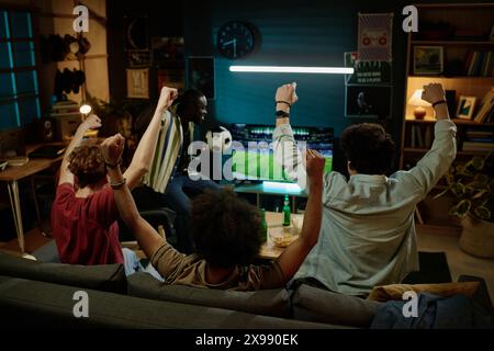 Rückansicht von vier jungen männlichen Freunden, die sich am späten Abend ein Fußballspiel im Fernsehen ansehen Stockfoto