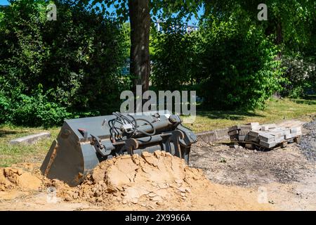 Baggerlöffel auf einem Erdhaufen und Reste von Straßenziegeln auf einer Holzpalette. Stockfoto