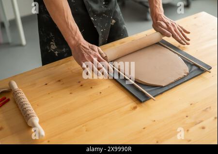 Nahaufnahme von Töpferhänden, die Ton ausrollen. Stockfoto