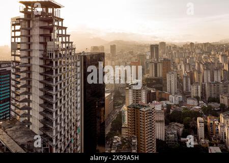 Blick aus der Vogelperspektive auf Caracas bei Sonnenuntergang mit dem David Tower Wahrzeichen Wolkenkratzer und Slums sichtbar. Drohnenaufnahme der venezolanischen Hauptstadt bei Sonnenuntergang. Konzept o Stockfoto