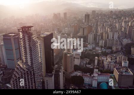 Blick aus der Vogelperspektive auf Caracas bei Sonnenuntergang mit dem David Tower Wahrzeichen Wolkenkratzer und Slums sichtbar. Drohnenaufnahme der venezolanischen Hauptstadt bei Sonnenuntergang. Konzept o Stockfoto