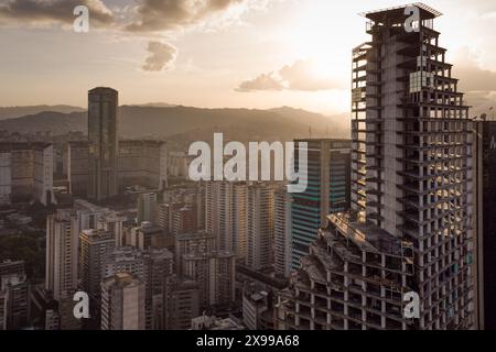 Blick aus der Vogelperspektive auf Caracas bei Sonnenuntergang mit dem David Tower Wahrzeichen Wolkenkratzer und Slums sichtbar. Drohnenaufnahme der venezolanischen Hauptstadt bei Sonnenuntergang. Konzept o Stockfoto