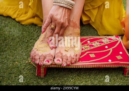 Die Füße der Braut sind mit komplizierten Henna- oder Mehndi-Mustern verziert, die im Rahmen der Haldi-Zeremonie bei einer traditionellen indischen Hochzeit mit Kurkuma bedeckt sind Stockfoto