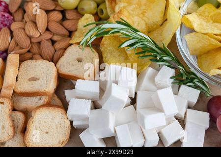 Mediterran inspirierte Platte mit Würfeln aus cremigem Fetakäse, knusprigen Mandeln, herzhaften grünen Oliven, Kartoffelchips und geröstetem Brot Stockfoto