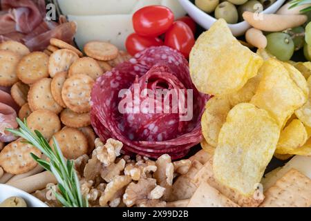 Wurstplatte mit einer Auswahl herzhafter Tapas: Ein Blumenarrangement aus Salamischeiben, knusprigen goldenen Kartoffelchips, Crackern und Nüssen Stockfoto