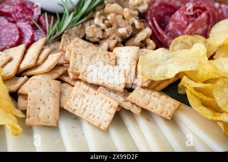 Snackplatte mit einer Auswahl an Crackern, Kartoffelchips, geräucherter Salami, Walnüssen und dünnen Käsescheiben, Teil einer größeren Wurstplatte Stockfoto