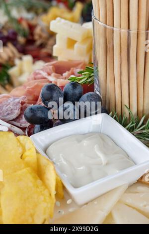 Wurstplatte mit einer reichhaltigen Auswahl an Snacks und Fingerfood: Dünne Scheiben von Räucherfleisch, knusprige Brotstangen, cremige Dip-Sauce Stockfoto