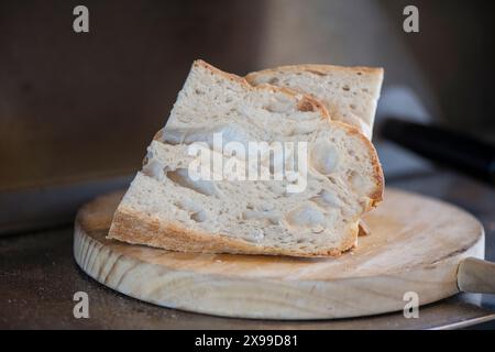 Ein paar Scheiben frisches Sauerteigbrot aus dem Ofen auf einem rustikalen Holzbrett, köstliches gebackenes Brot mit einer schönen Textur und einer goldenen Kruste Stockfoto