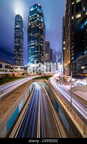 Wolkenkratzer und Straßenverkehr mit unscharfen Lichtspuren bei Nacht, Hongkong, China Stockfoto