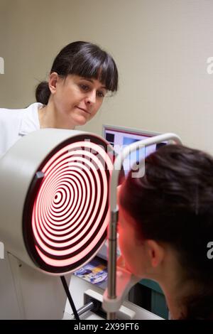 Augenuntersuchung Patient mit einer Hornhauttopographie, die am Auge gemessen wird. Das Gerät in der Mitte projiziert helle Ringe auf das Auge, die durch Untersuchung der Reflexion in seiner Oberfläche reflektiert werden. die Hornhaut ist der vordere Teil des Auges, der Iris und Pupille bedeckt. Sie ist für den Großteil der Lichtfokussierung verantwortlich. da nur eine feine Fokussierung durch die Linsendefekte in Form der Hornhaut zu einer Vielzahl von Fokussierungsstörungen führen kann, können diese operativ oder durch das Tragen von maßgeschneiderten Kontaktlinsen oder spect behandelt werden Stockfoto