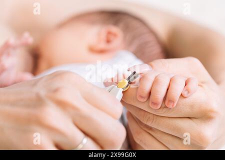 Nahaufnahme einer Mutter, die vorsichtig die Fingernägel ihres Neugeborenen trimmt, um versehentliches Kratzen zu vermeiden Stockfoto