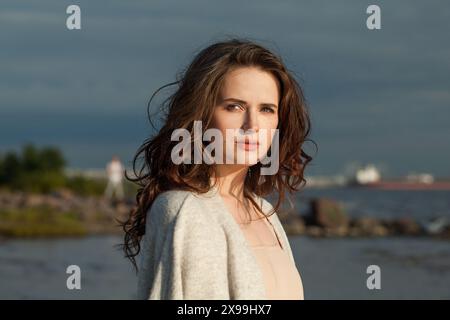 Melancholisch brünette Frau mit frischer Haut, natürlichem Make-up und gesundem, welligen braunen Haar genießt die sonnige Morgen- und Meeresluft. Innenmodell Außenausführung fa Stockfoto