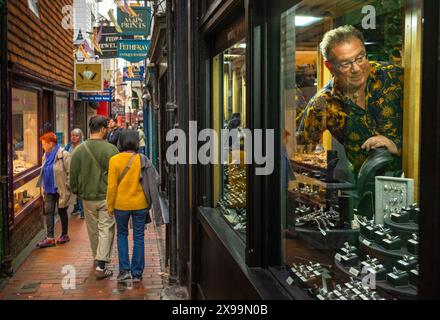 Shopper gehen an einem Mann vorbei, der in seinem Geschäft im Lanes Conservation Area in Brighton, East Sussexc, Großbritannien, Schmuck arrangiert. Stockfoto