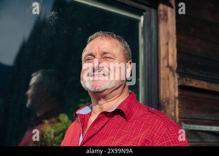 Älterer Mann mit einem sanften Lächeln, der die Wärme der untergehenden Sonne genießt Stockfoto