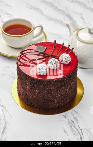 Teezeit mit rot glasiertem Schokoladenkuchen mit Kokos-Trüffeln Stockfoto