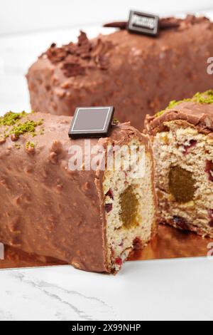 In Scheiben geschnittener, mit Schokolade überzogener Brotkuchen mit Fruchtgelee, getrockneten Preiselbeeren und Pistazien Stockfoto