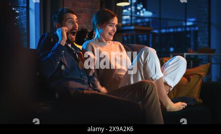 Porträt eines wunderschönen Paares, das zu Hause auf einer Couch sitzt und in ihrem stilvollen Loft Apartment eine gruselige TV-Show ansieht. Mann und Frau streamen Horrorfilm und werden erschreckt und überrascht. Stockfoto