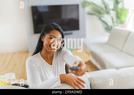Schwarze Frau, die zu Hause Fernsehen schaut, sitzt auf dem Sofa Stockfoto