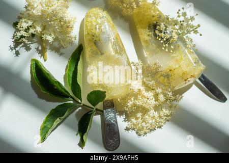 Gefrorene weiße Holunderblüten in Wasser in Form von Eis auf einem weißen Tisch. Stockfoto