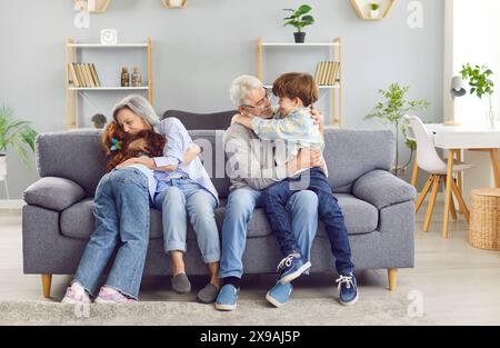 Porträt von Großeltern, die mit ihren Enkeln zu Hause auf dem Sofa sitzen und sich umarmen. Stockfoto