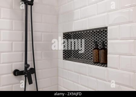 Moderne, weiß geflieste Dusche mit schwarzen Armaturen und eingebautem Regal Stockfoto