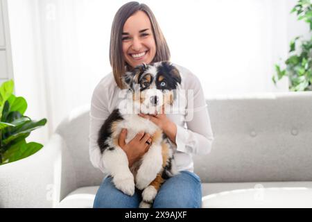 Hübsche Frau mit ihrem australischen Berger-Welpen auf dem Sofa Stockfoto