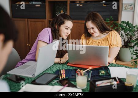 Lächelnde Frau, die ihren Laptop mit ihrer Schwester teilt, die zu Hause an Down-Syndrom leidet Stockfoto