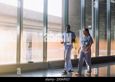 Aufnahme in voller Länge von glücklichen medizinischen Fachleuten, die während des Spazierens im Krankenhaus diskutieren Stockfoto