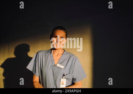 Porträt einer lächelnden älteren Ärztin, die vor der Wand im Krankenhaus steht Stockfoto